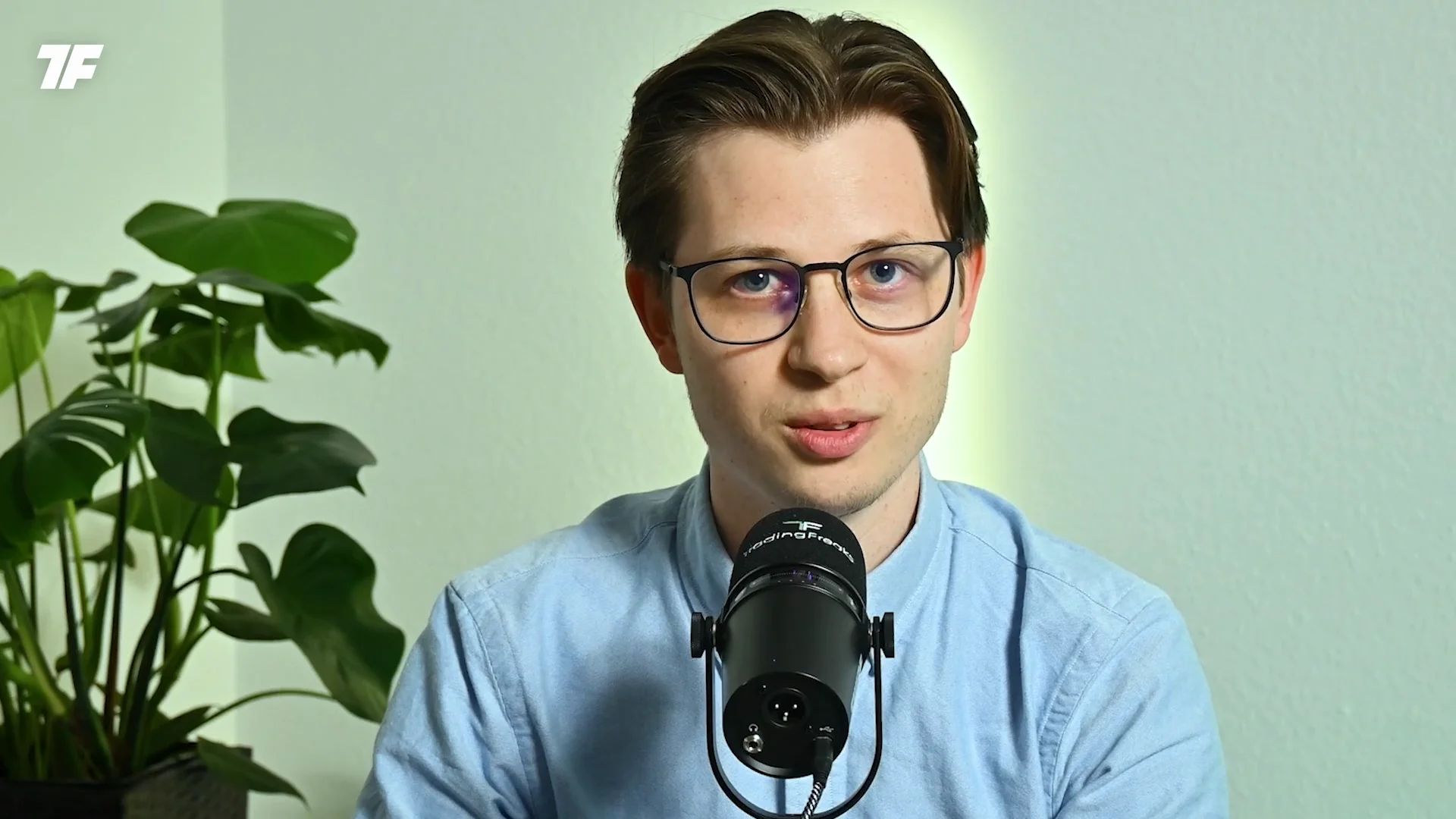 Mann mit Brille spricht in ein Mikrofon vor einer hellen Wand; Top Trader Programm-Text links.